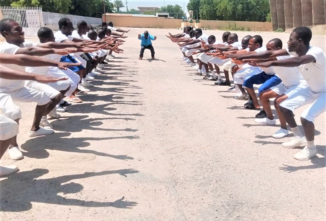 Recruits in white training kit performing squats in formation
